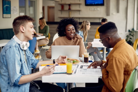 A group of male and female students discuss their textbooks over lunch at the university canteen