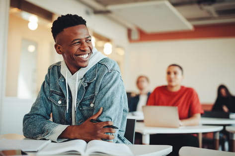 A male student sitting at his desk smiles off-camera in a university seminar room